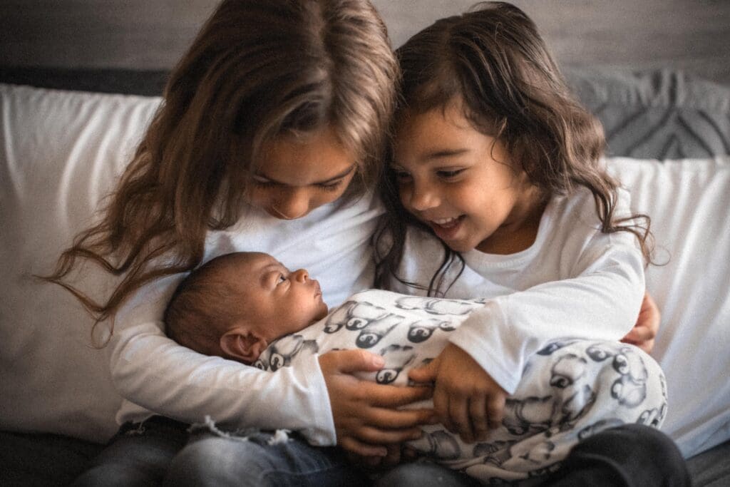 siblings smiling at baby during newborn photography session in Sacramento, CA